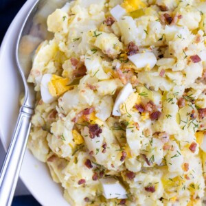 Instant Pot potato salad with bacon and eggs is served from a white bowl with a spoon.
