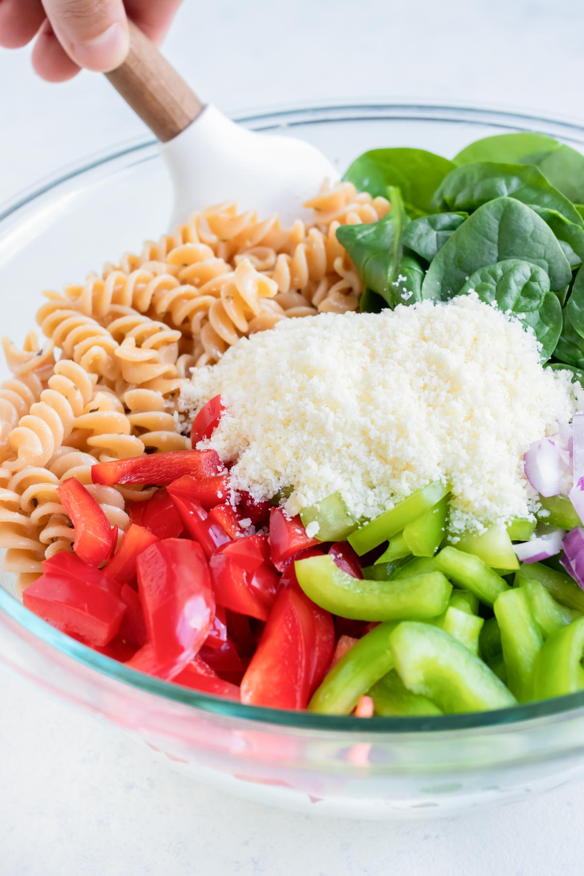Chopped peppers, spinach, and Parmesan cheese are added to a bowl of noodles with Italian dressing.