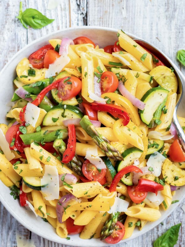 A large white bowl full of an easy and healthy roasted vegetable pasta with tomatoes, asparagus, and bell peppers.