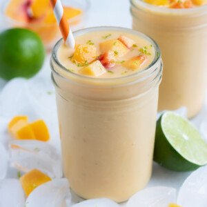 Two glasses are used to hold a thick and creamy peach banana smoothie.