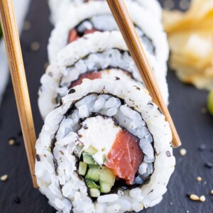 Chopsticks are used to pick up a homemade Philadelphia Sushi roll piece.