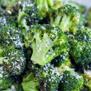 Roasted air fryer broccoli is served in a white bowl with Parmesan cheese and lemon zest on top.