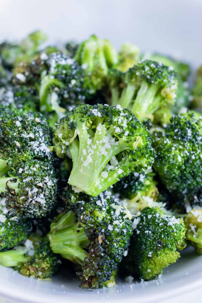 Roasted air fryer broccoli is served in a white bowl with Parmesan cheese and lemon zest on top.