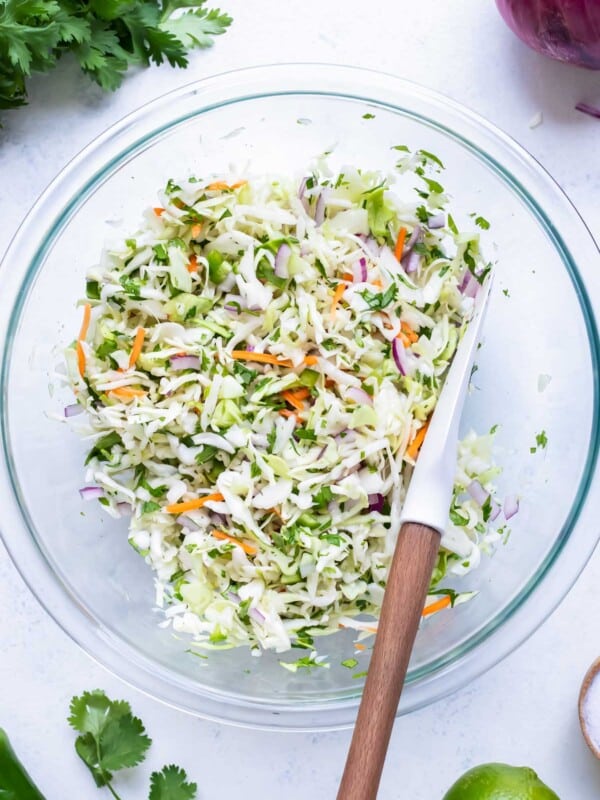 A glass bowl is filled with cabbage and other ingredients for this taco slaw.