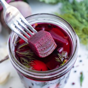 A fork scoops a pickled beet cube out of the jar.