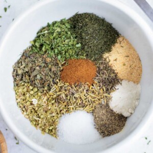 Spices and herbs are in a white bowl for a Greek seasoning recipe.