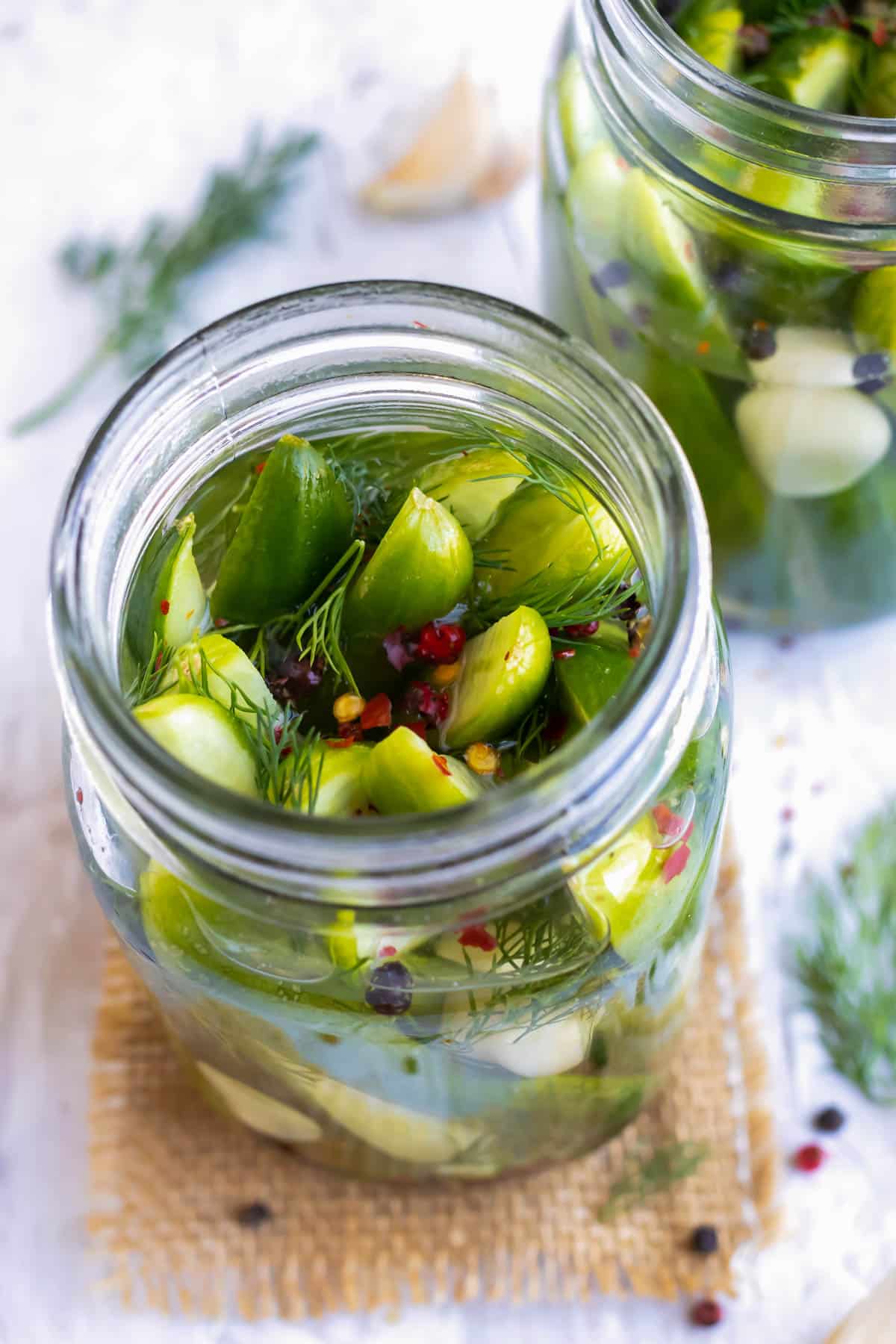 Pickles, dill, and peppercorns are in a jar with pickling solution.
