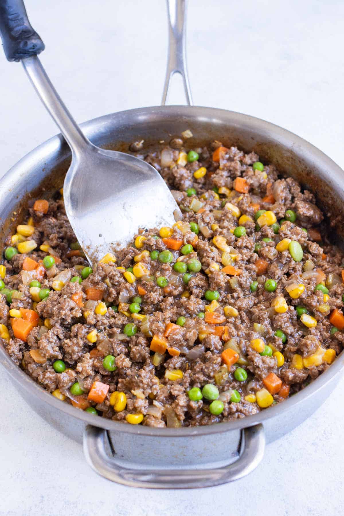 A spatula stirs a meat and vegetable filling.