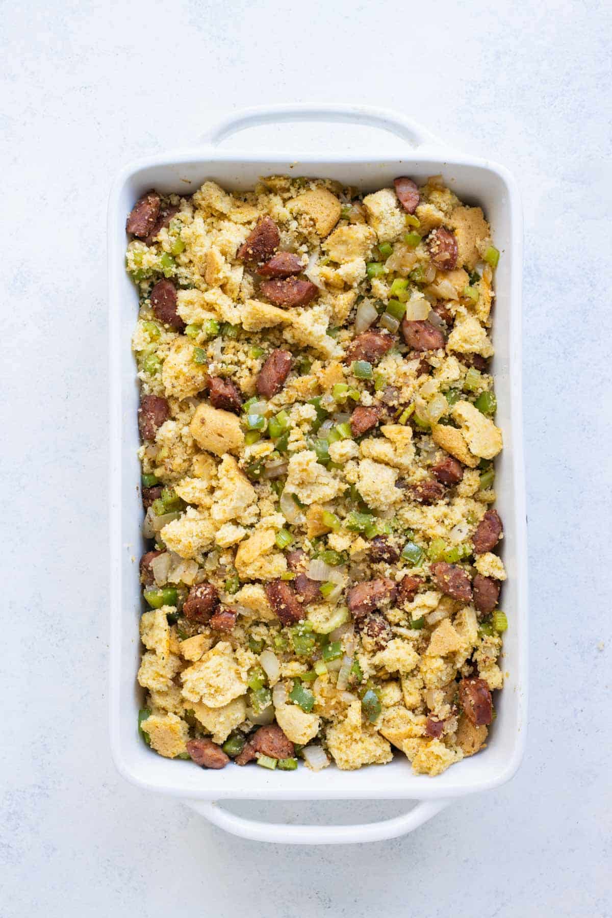 A white baking dish is full of southern cornbread with sausage.