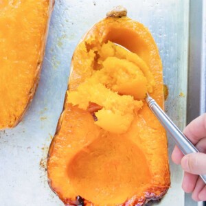 A spoon scooping out the flesh from a roasted butternut squash.