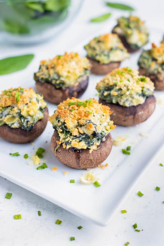 Crisp and golden brown spinach artichoke mushrooms are served on a platter with chives.