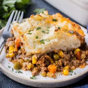 A piece of a traditional shepherd's pie recipe on a white plate with a fork for a weeknight dinner.