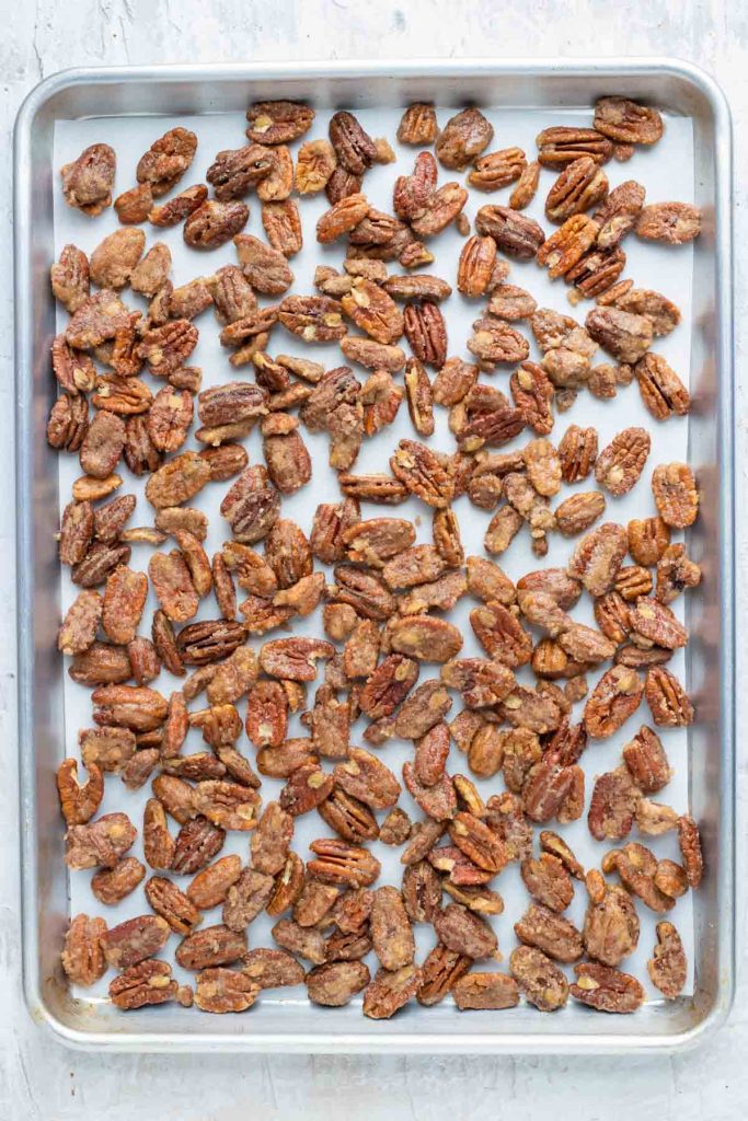 Cinnamon spiced pecans on a large baking sheet before being roasted in the oven.