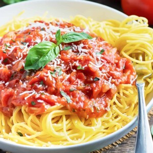 A white bowl full of spaghetti with pasta pomodoro sauce and basil.