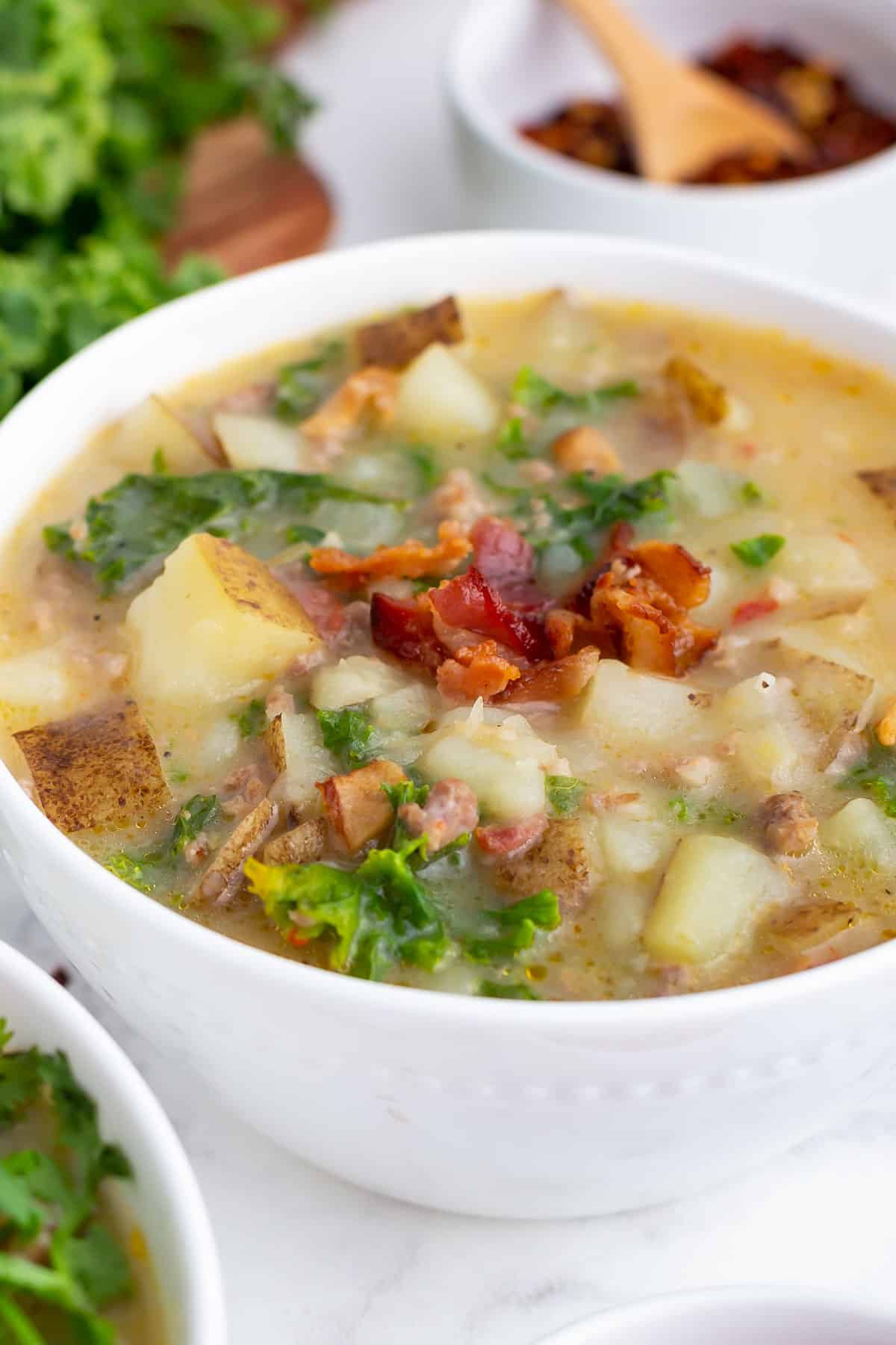 A bowl full of a copycat Olive Garden Zuppa Toscana is in a white bowl with bacon, potatoes and kale.