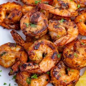 Blackened shrimp on a white plate with lemon wedges.