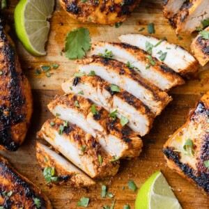 A chipotle chicken copycat recipe is on a cutting board and cut into strips with cilantro and lime wedges.