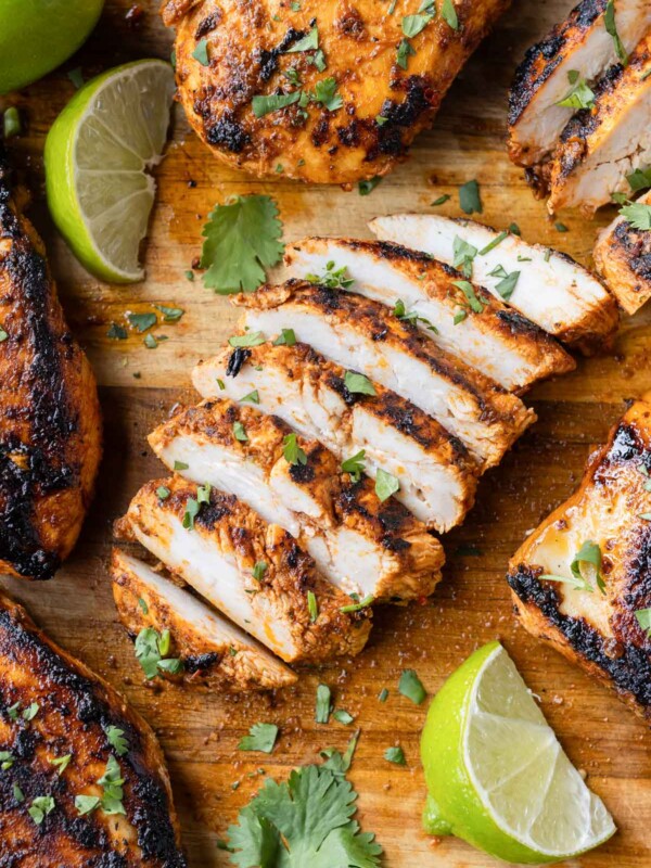 A chipotle chicken copycat recipe is on a cutting board and cut into strips with cilantro and lime wedges.