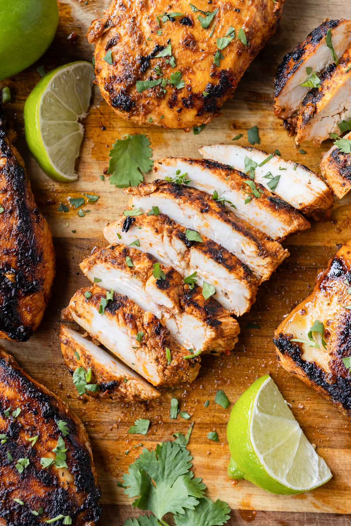 A chipotle chicken copycat recipe is on a cutting board and cut into strips with cilantro and lime wedges.