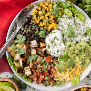 A white bowl is cull of a Chipotle Burrito Bowl copycat recipe that was made at home with chipotle chicken, corn salsa, fresh tomato salsa, and cilantro lime rice.