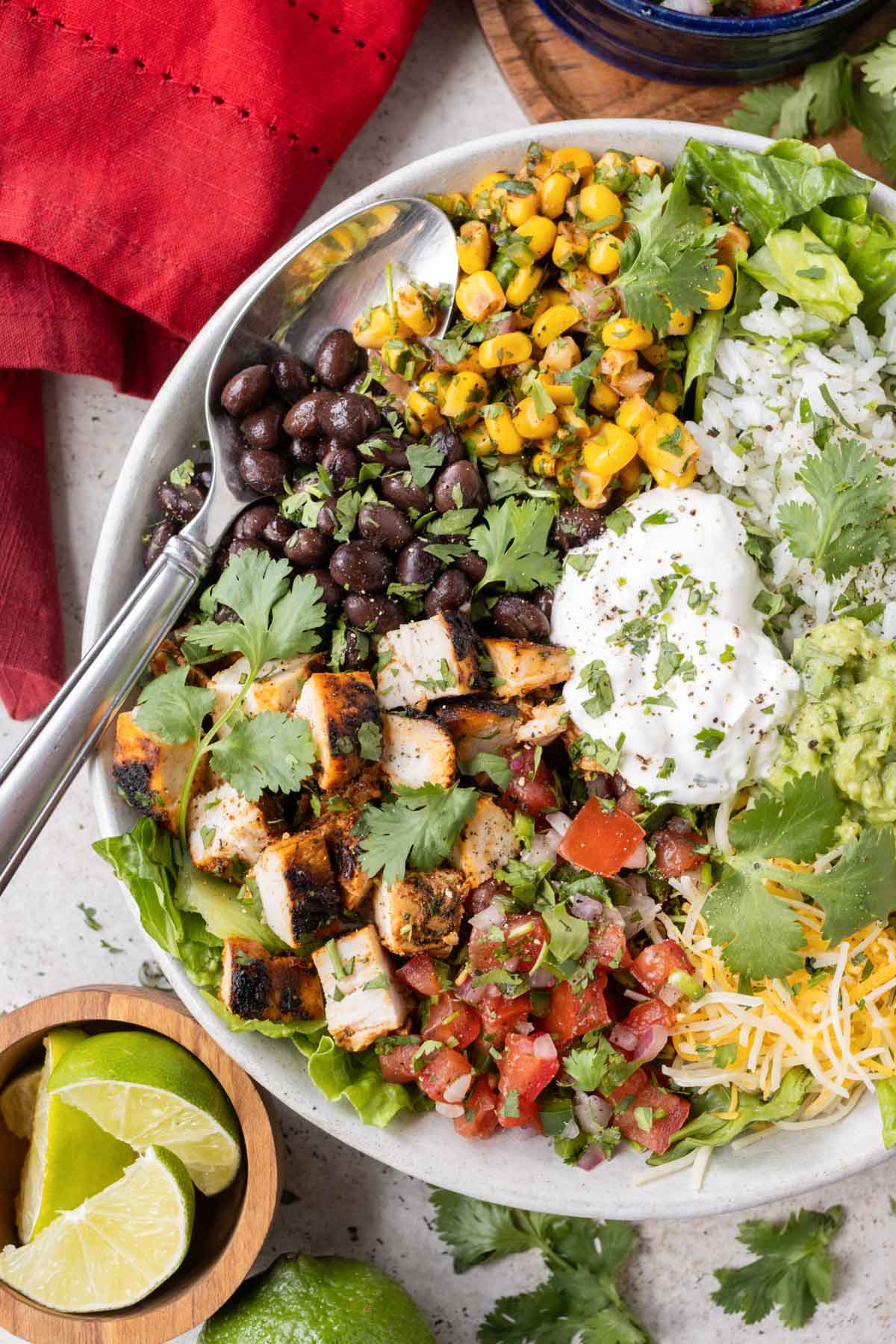 A spoon is scooping up a bite of a Chipotle burrito bowl made at home with copycat chipotle chicken, corn salsa, cilantro lime rice, and black beans.