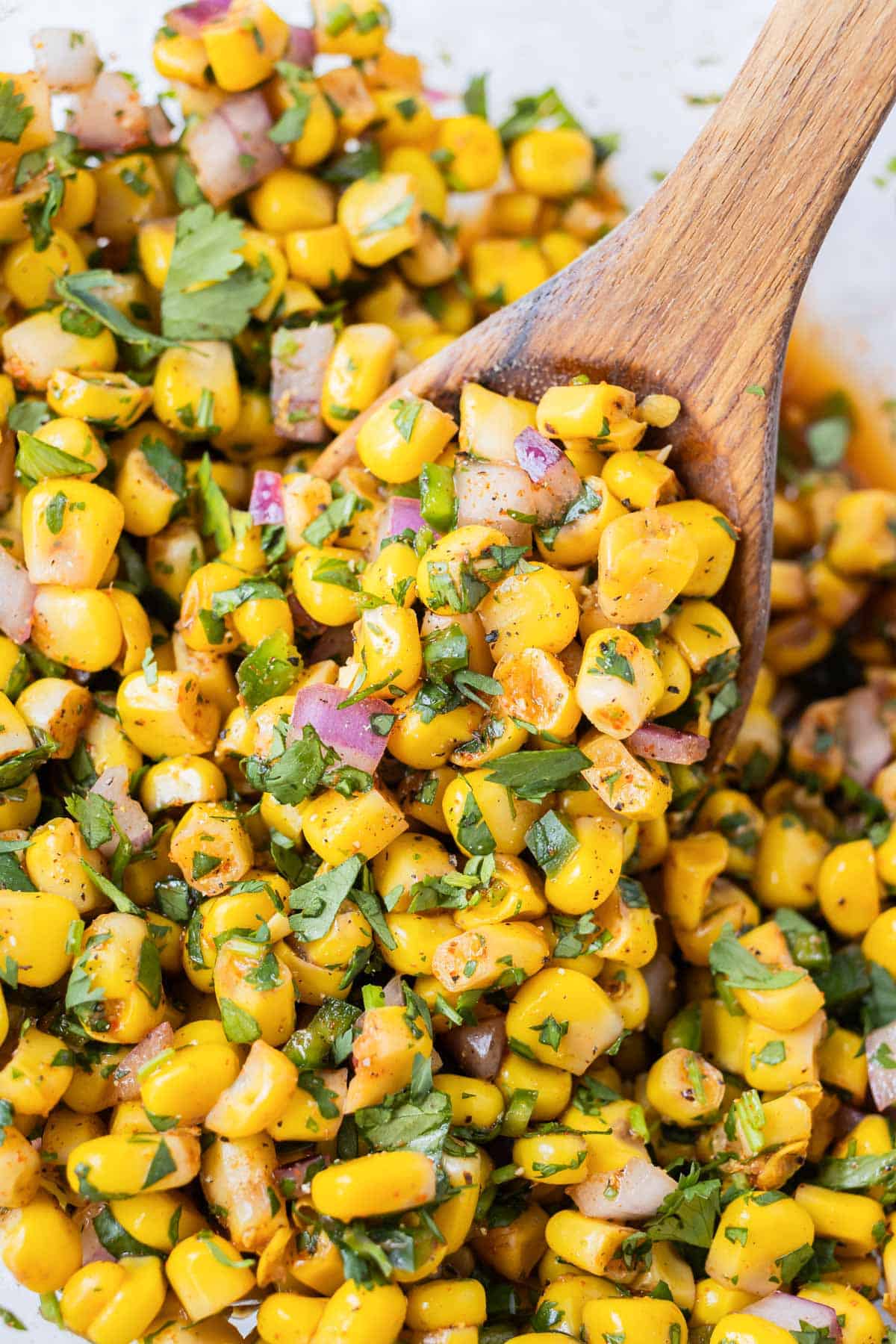 A wooden spoon scooping up some Chipotle Corn Salsa from a mixing bowl.