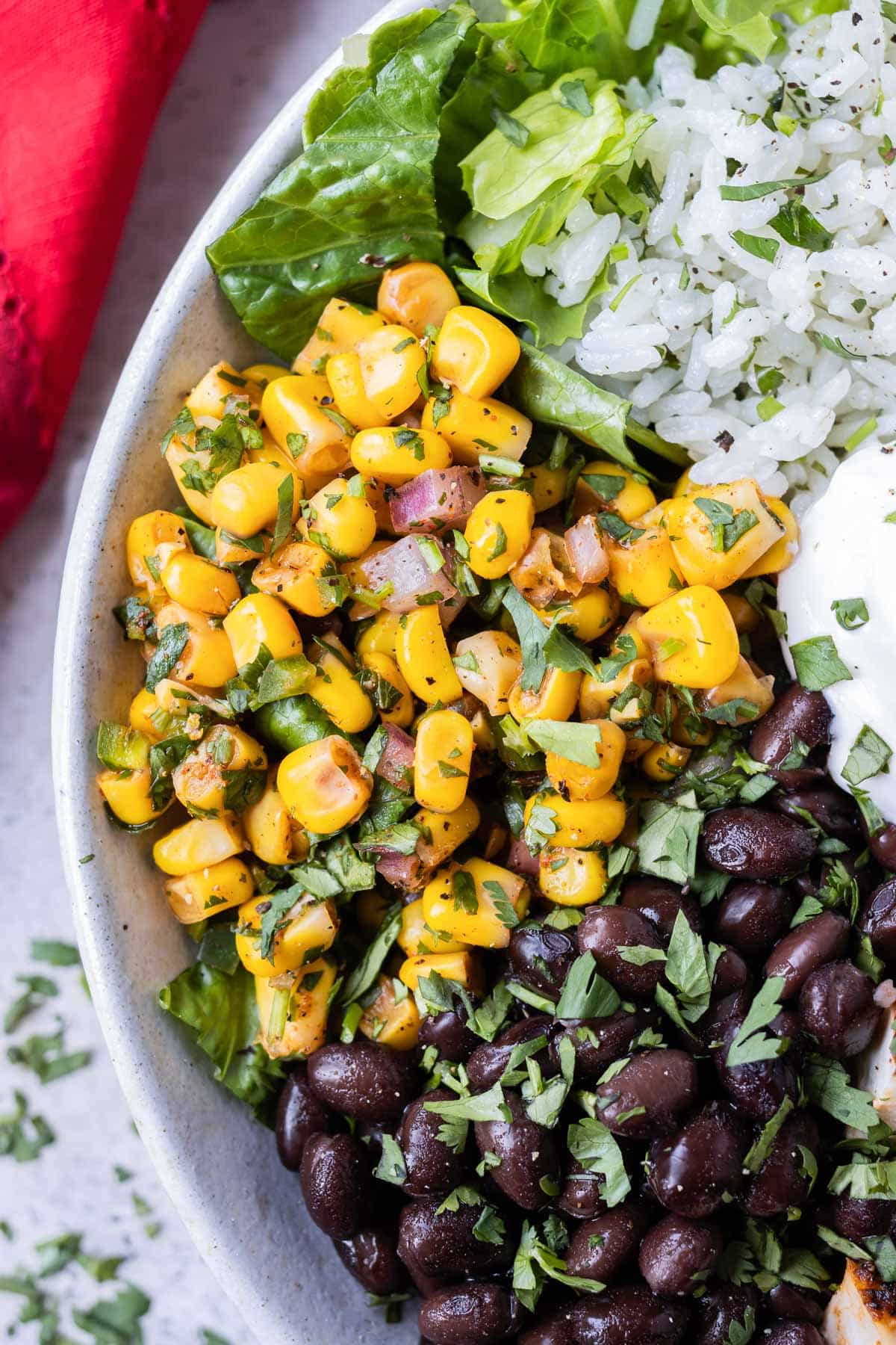 A serving of Chipotle Corn Salsa is in a chicken burrito bowl next to black beans and cilantro lime rice.