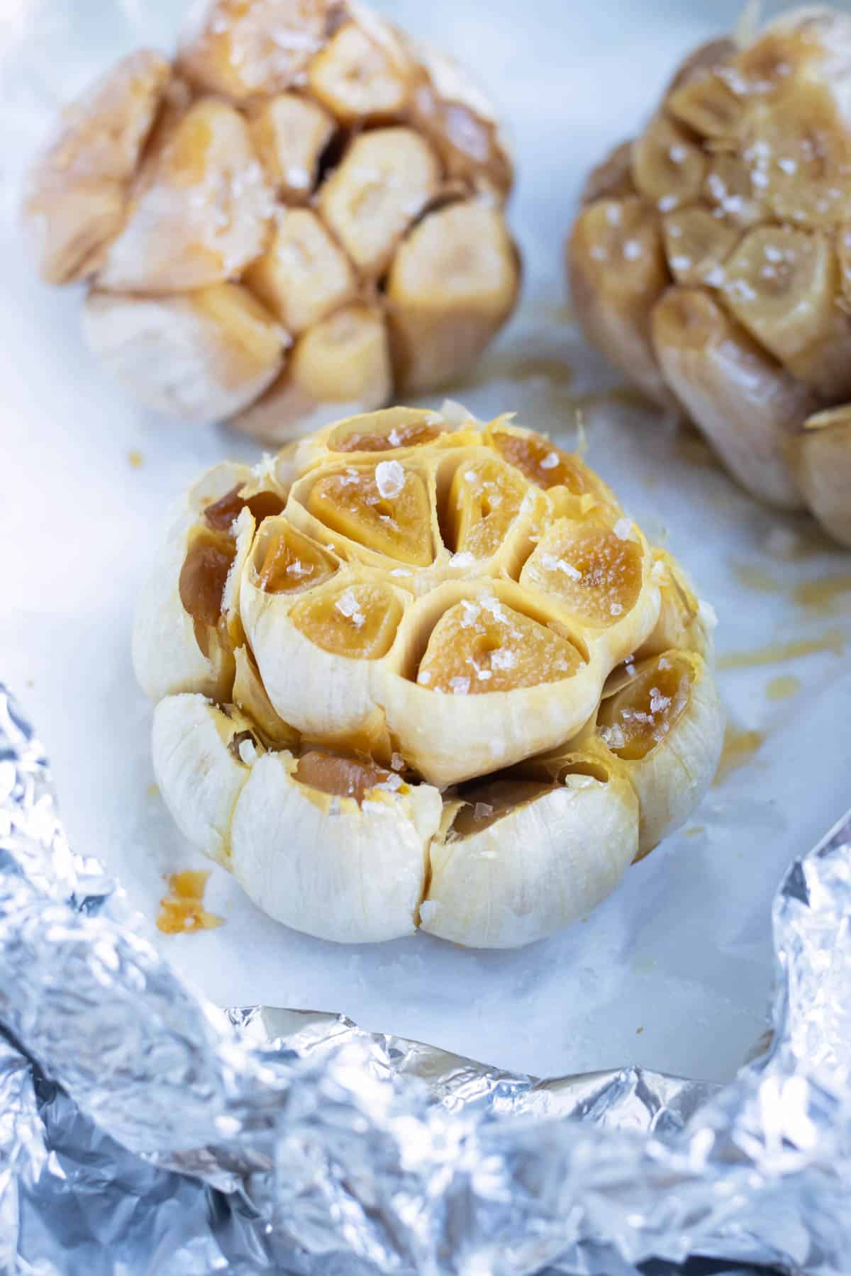 A head of roasted garlic is on a piece of parchment paper after baking in the oven.