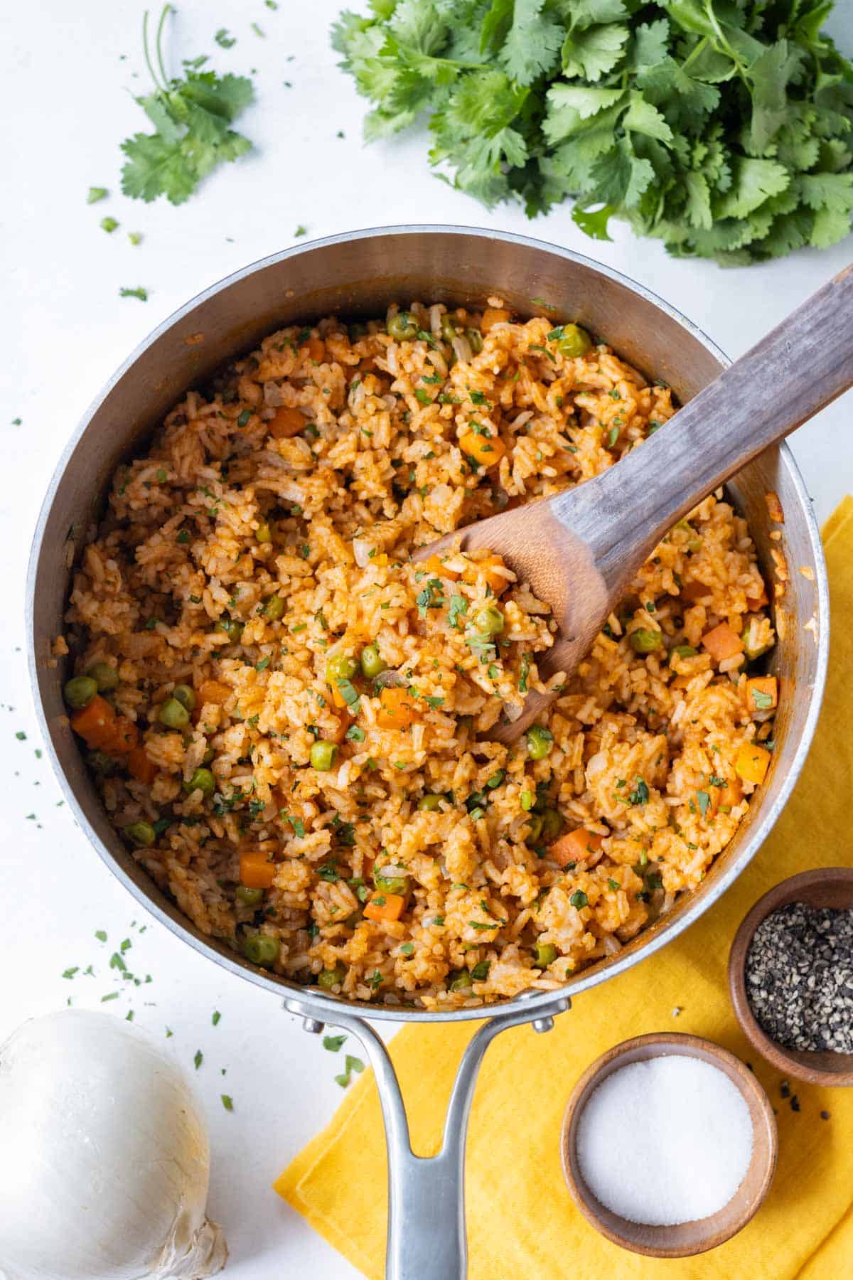 A metal pot full of an authentic Mexican rice recipe has a wooden spoon in it.