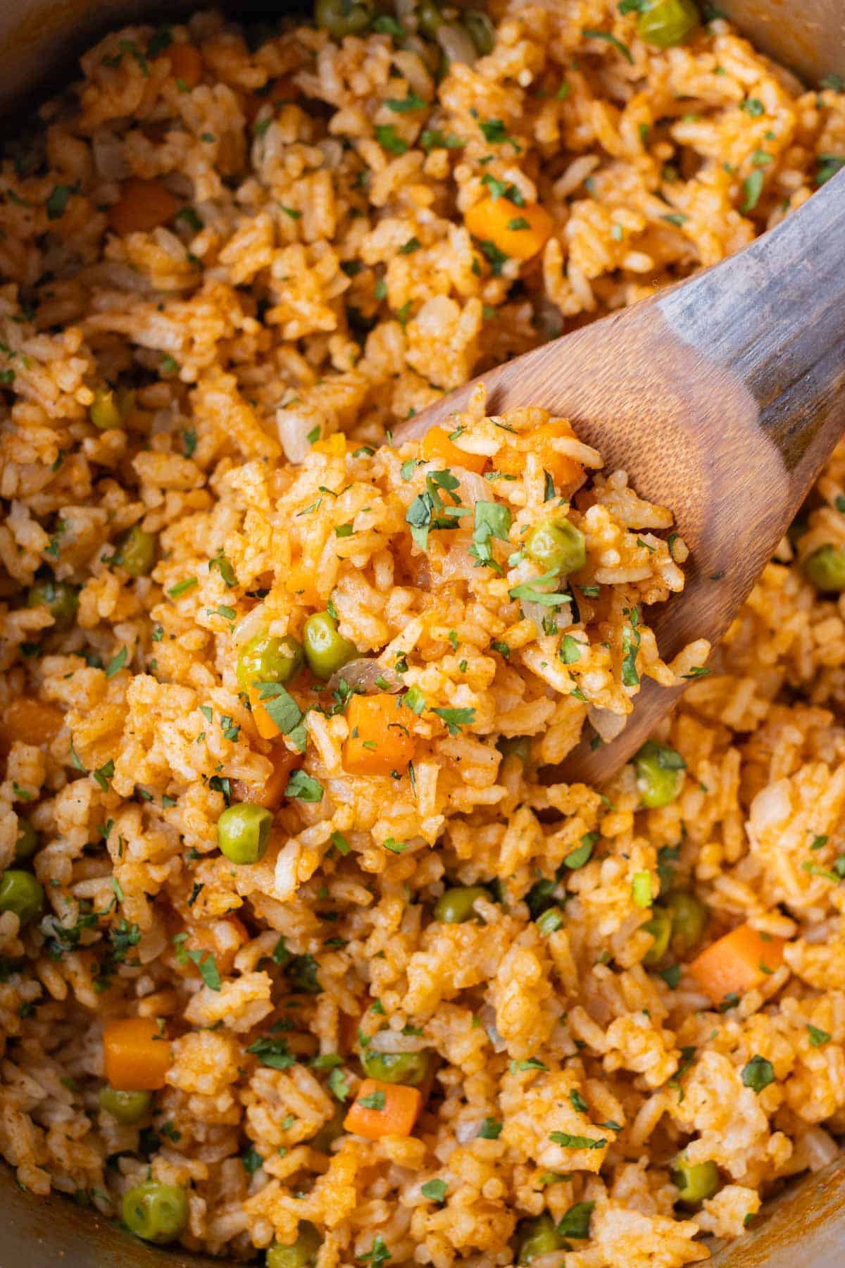 A wooden spoon is scooping up a bite of restaruant-style Mexican rice.