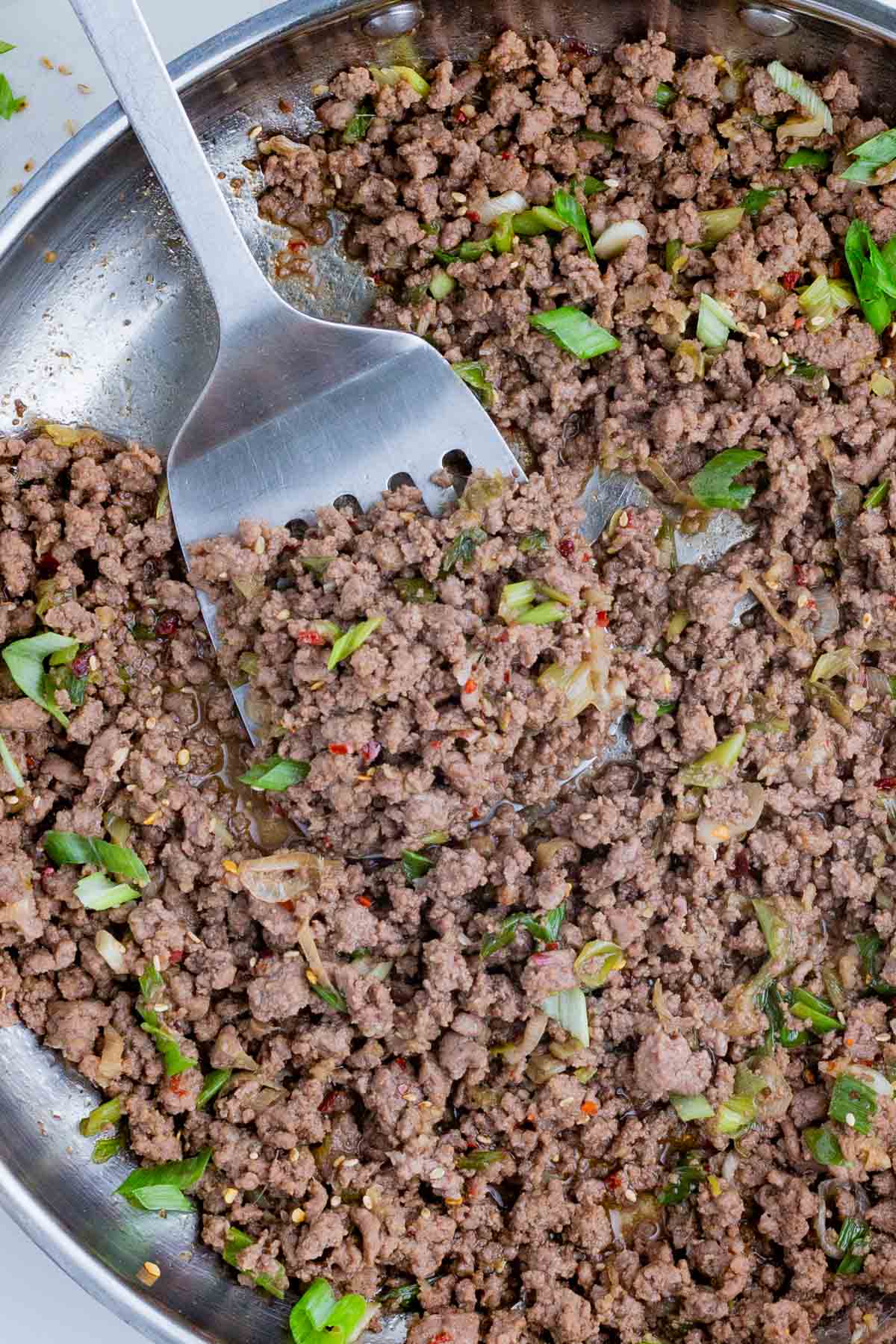 A spatula stirs the seasoned beef in a pan.