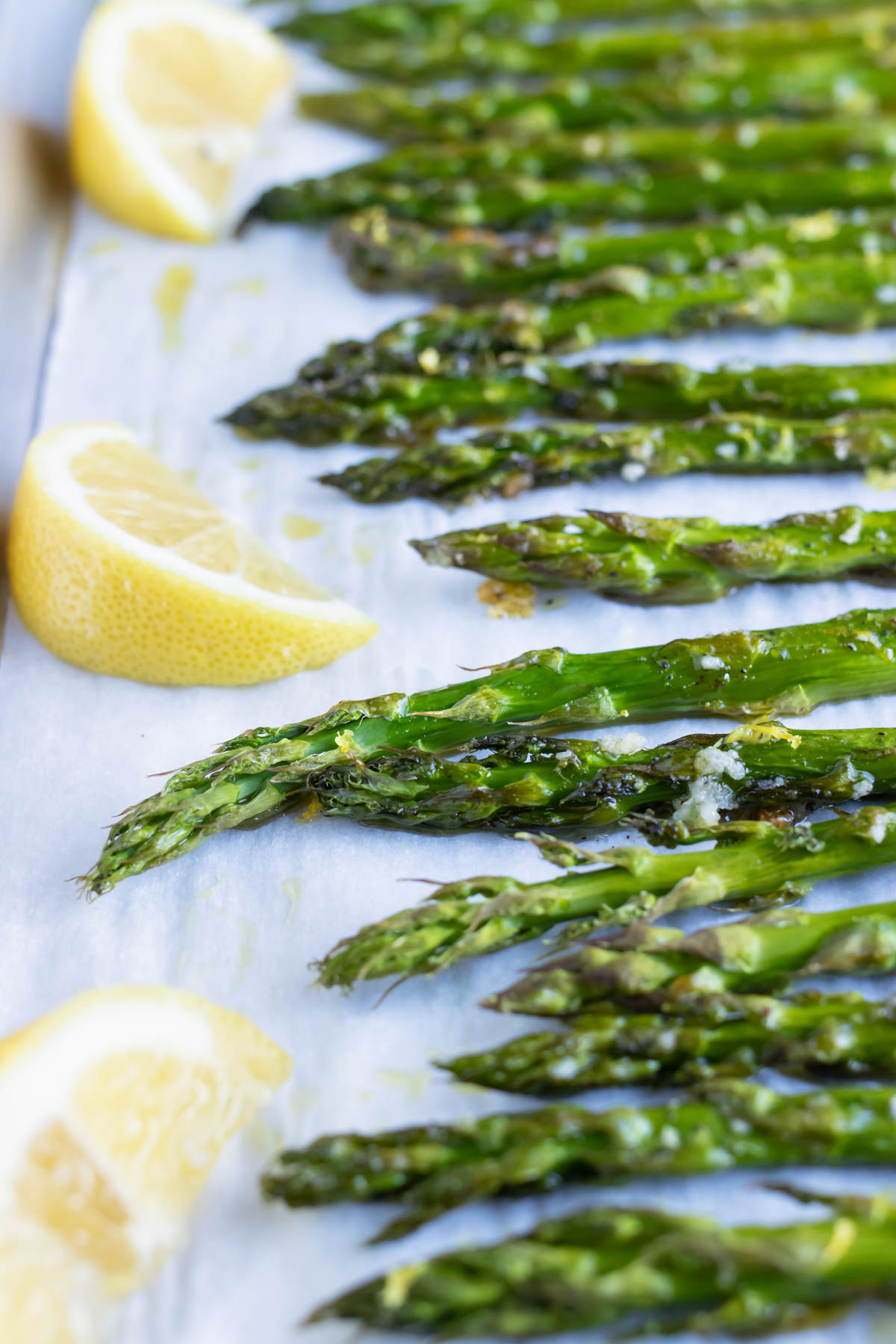 Roasted asparagus spears on a baking sheet with lemon wedges.