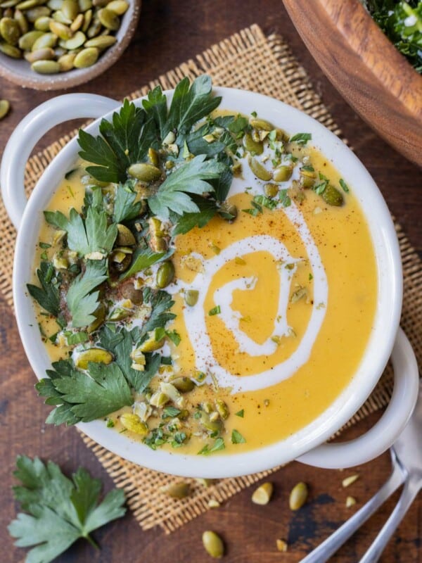 A bowl full of roasted butternut squash soup with coconut milk that's garnished with pumpkin seeds and parsley leaves.