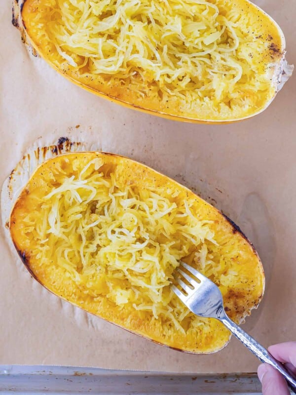 A baked spaghetti squash half being shredded using a fork after roasting.