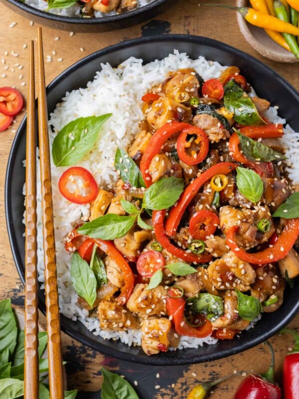 An authentic Thai Basil Chicken recipe is served with red bell peppers on basmati rice with chopsticks.