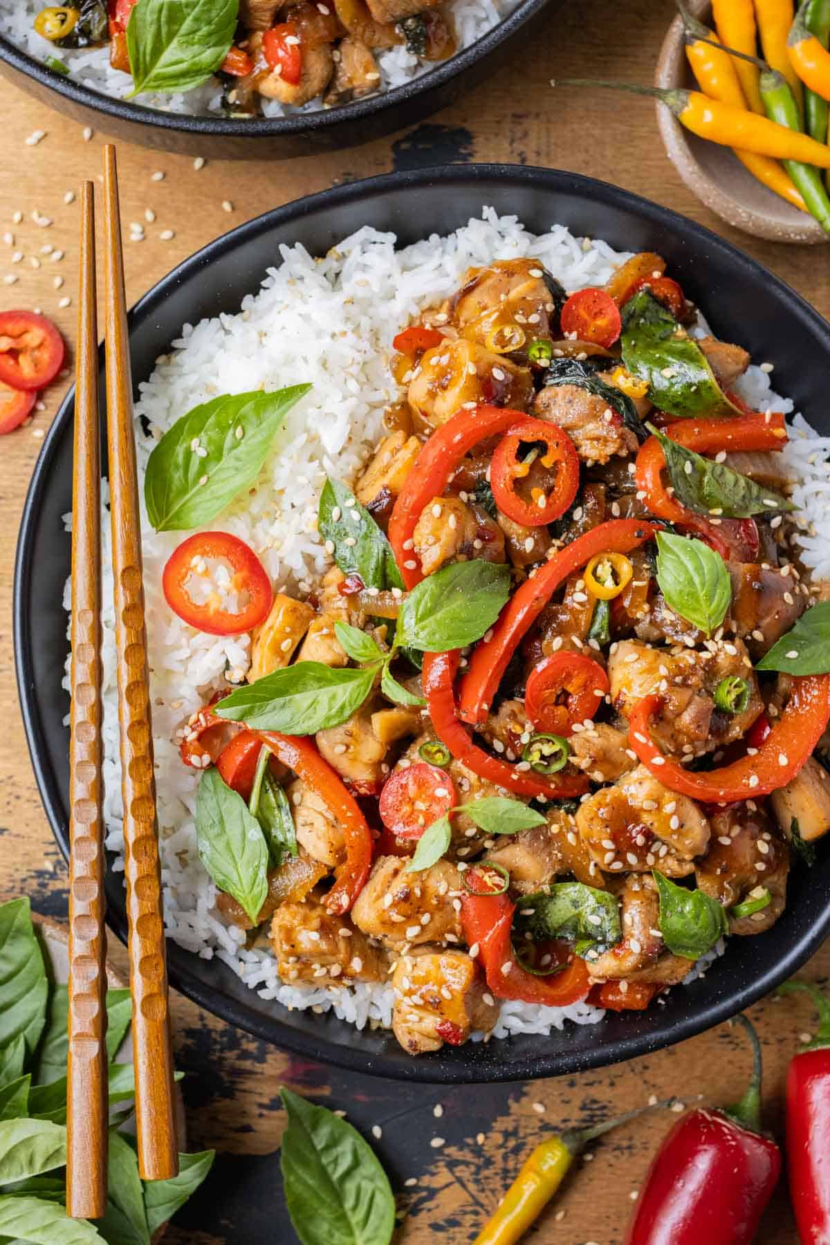 An authentic Thai Basil Chicken recipe is served with red bell peppers on basmati rice with chopsticks.