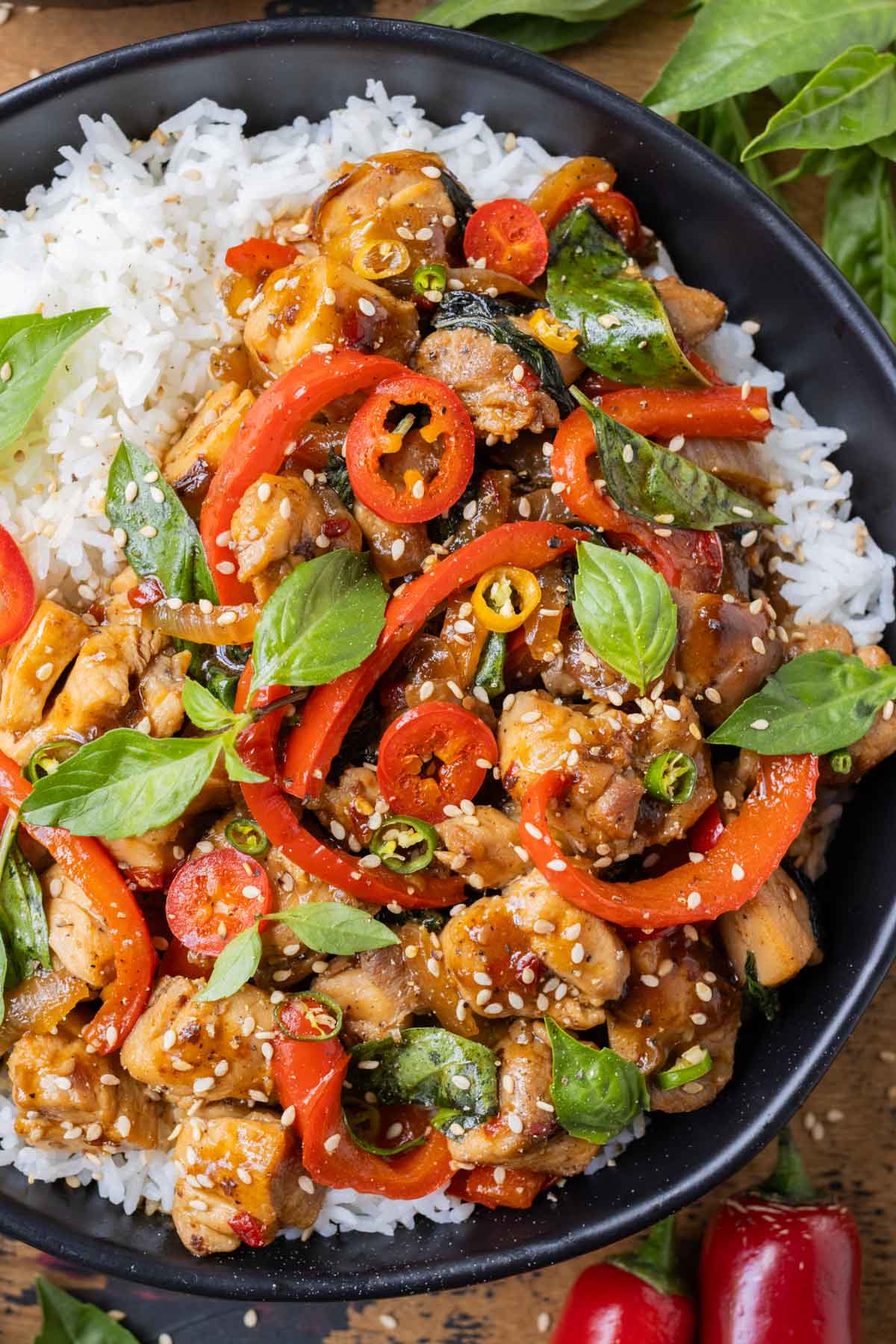 A black bowl full of Thai basil chicken over rice.