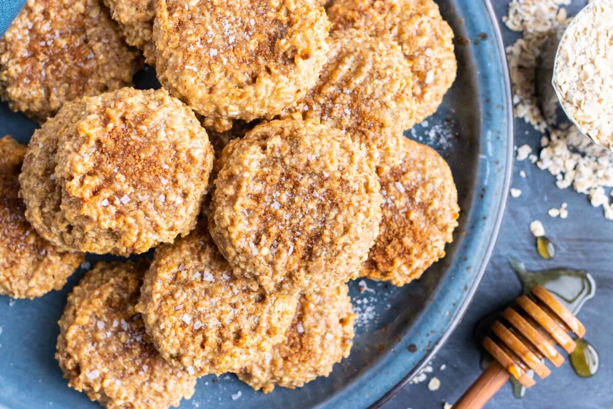 Almond butter oatmeal cookies are on a blue serving plate with honey and oats next to it.