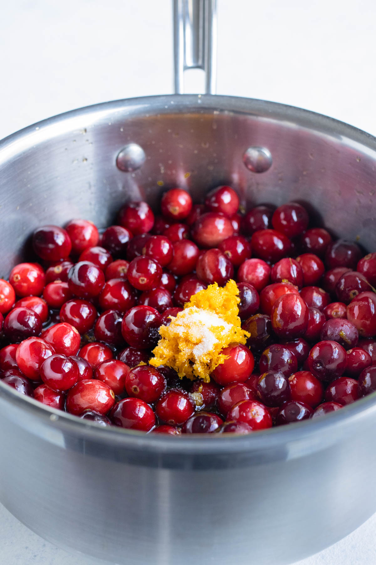 Whole cranberries, orange zest, and salt are added to the pot.