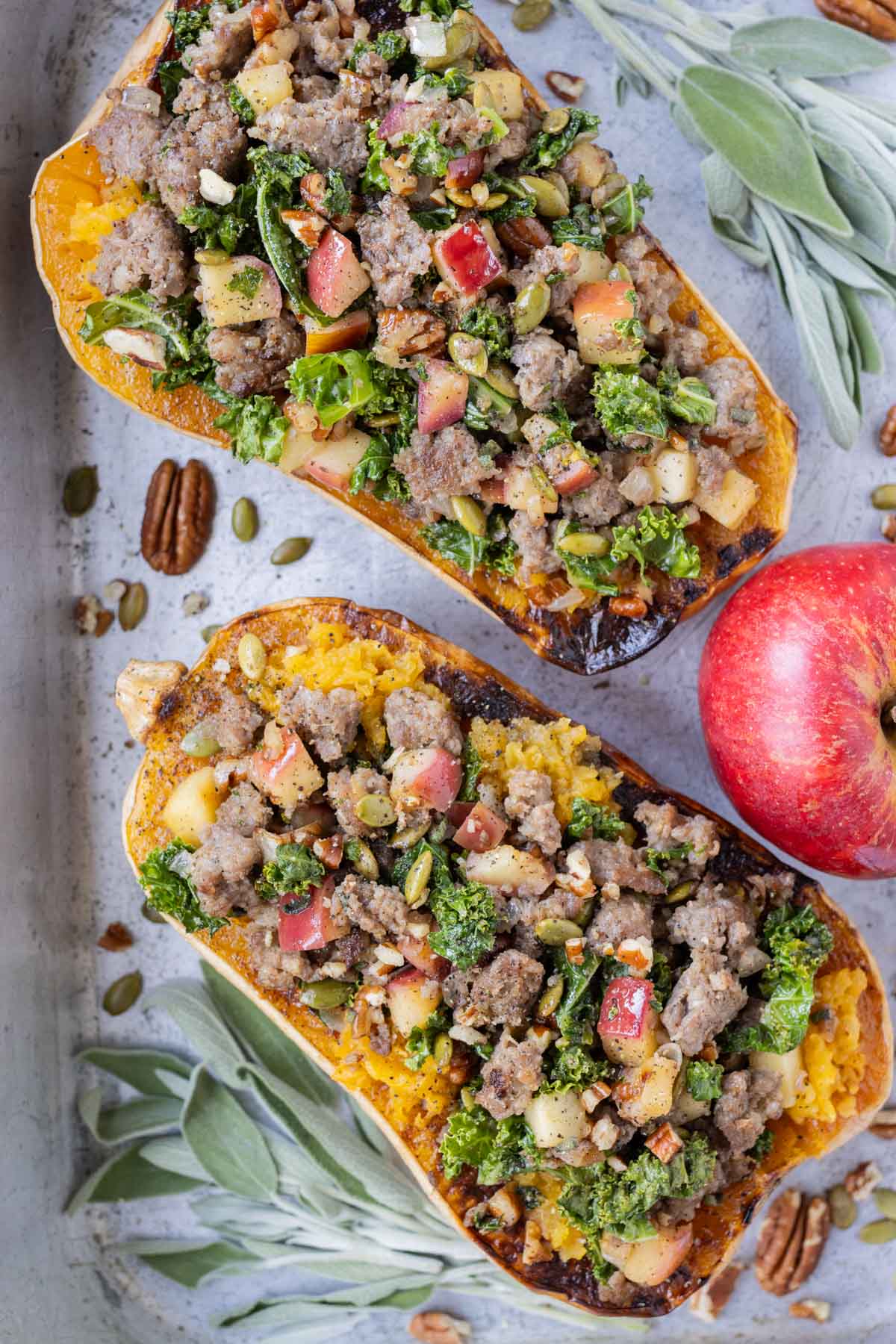 Sausage Stuffed Butternut Squash RECIPE on a sheet pan with fresh apples.