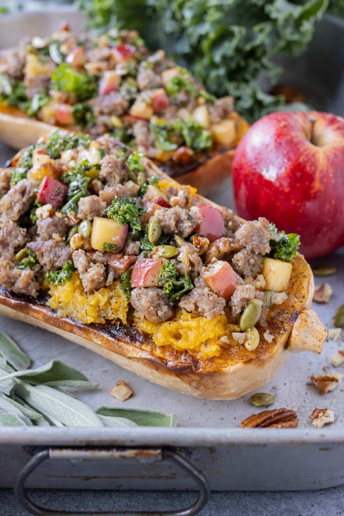 Ground sausage stuffed butternut squash recipe for Fall next to an apple and a bunch of kale.