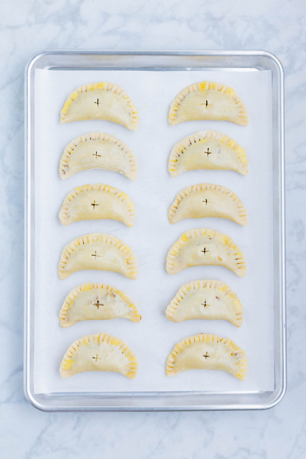 Hand pies are lined up on a baking sheet before baking.