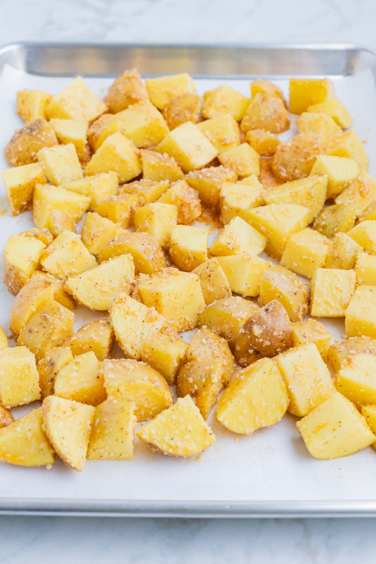 Seasoned potatoes are spread on a baking sheet.