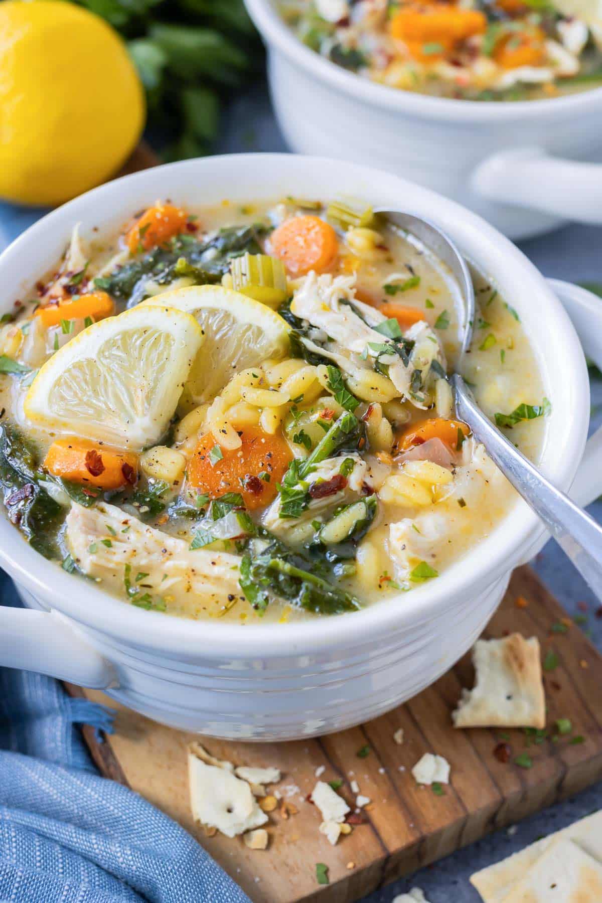 Two soup bowls are full of Lemon Chicken Orzo Soup and topped with lemon wedges.