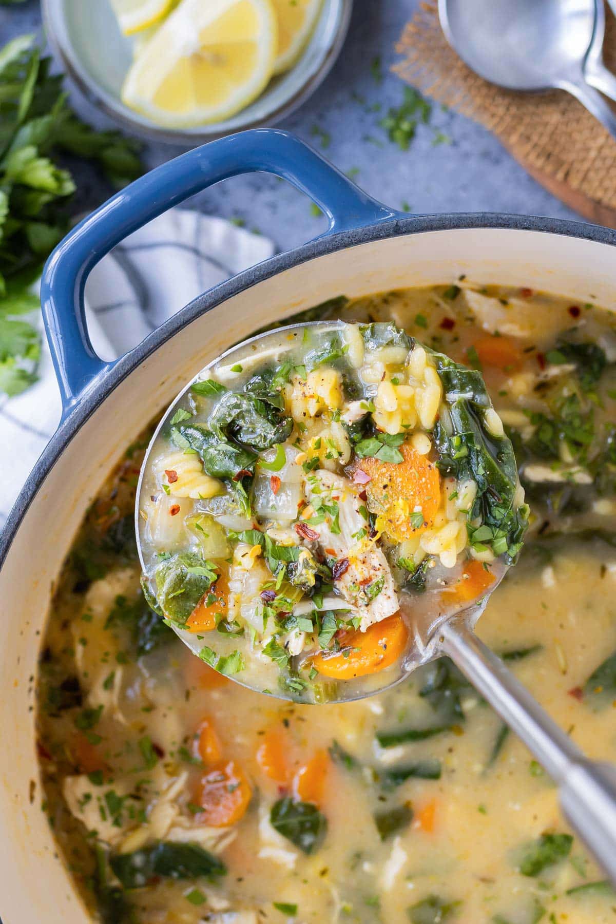 A ladle scoops a serving of Lemon Chicken Orzo Soup from a Dutch oven.