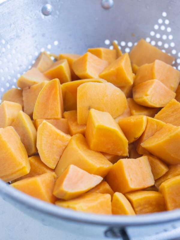 Cubed and tender boiled sweet potatoes are drained in a colander.