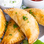 Empanadas are served on a plate with salsa, sour cream, and guacamole.