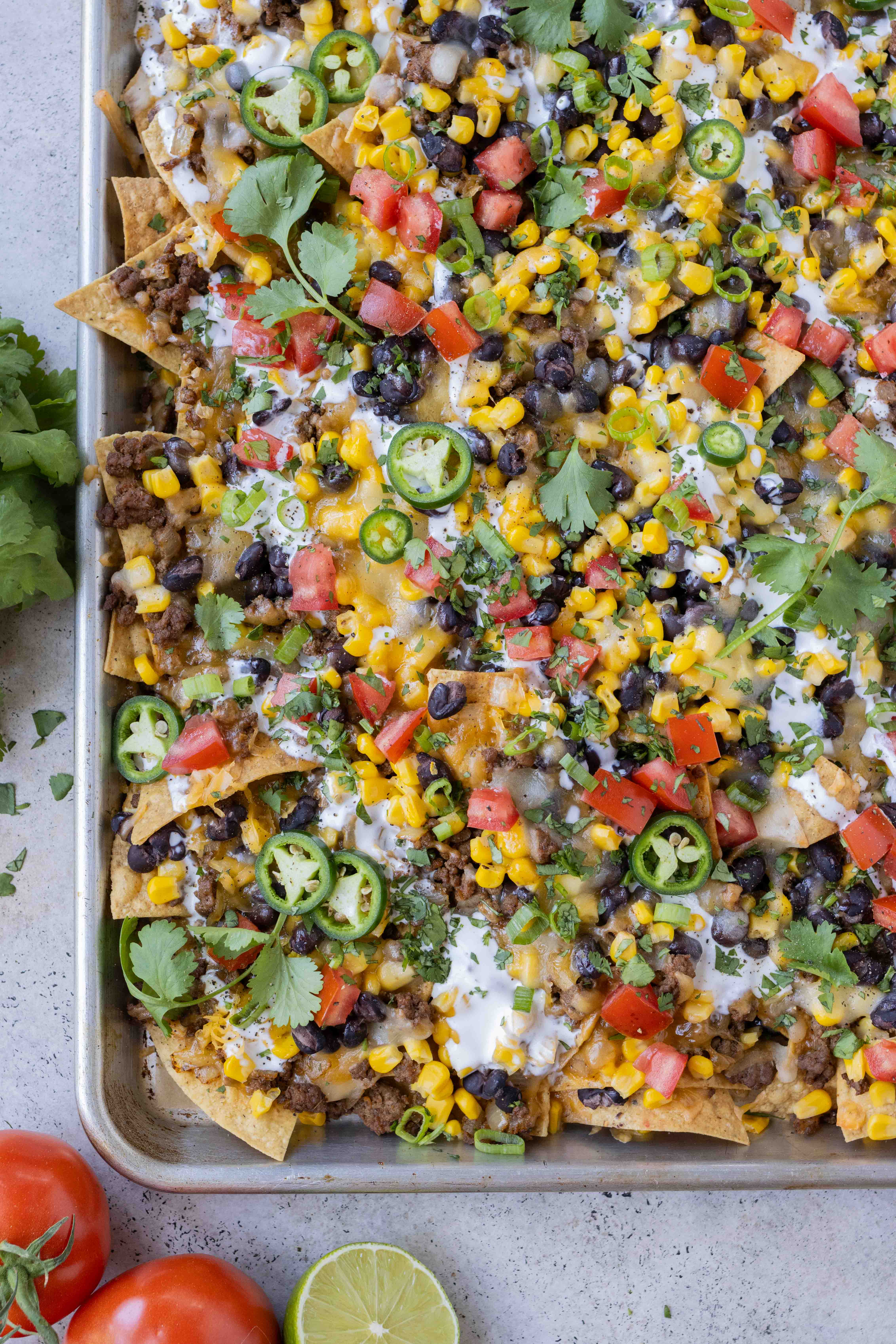 Chips are spread on a baking sheet and topped with cheese, meat, and beans for the perfect sheet pan nachos.