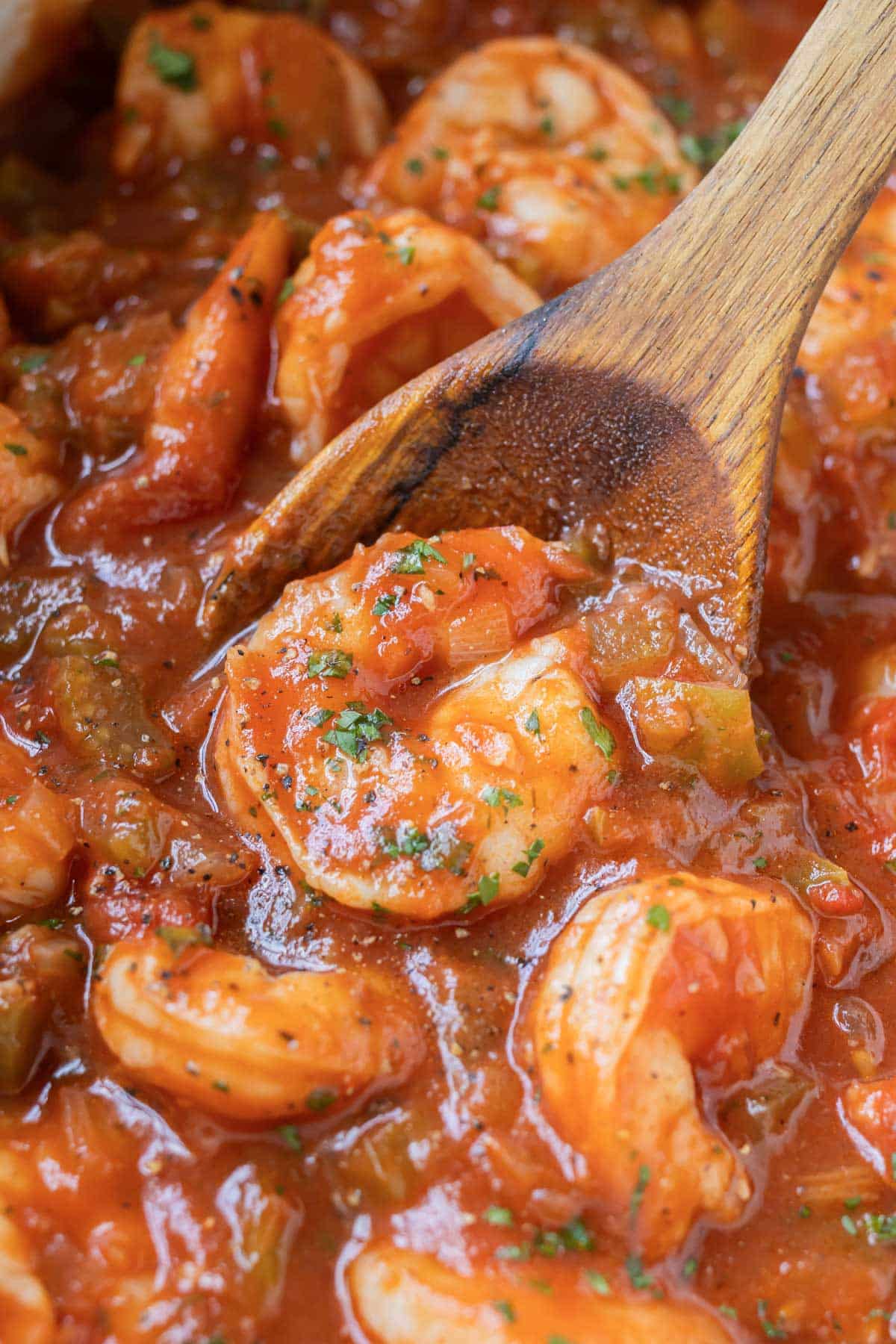 A wooden spoon is scooping up a serving of an authentic New Orleans-style Shrimp Creole recipe from a Dutch oven.