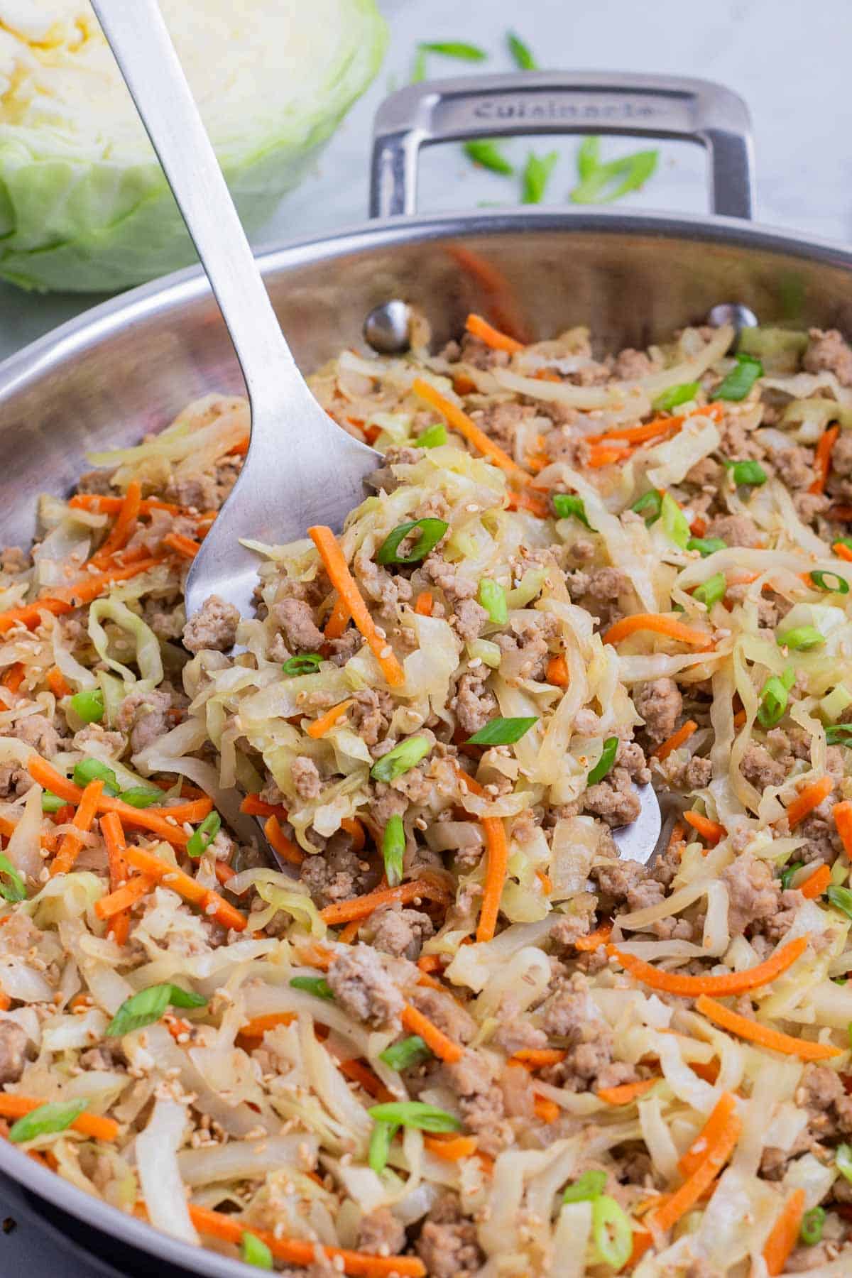 A spatula scoops up a serving of an egg roll bowl from a large skillet.